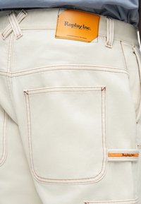 Λευκά υφασμάτινα παντελόνα με πορτοκαλί ραφές και λογότυπο. Διαθέτει μία πίσω τσέπη και επιπλέον τσέπη χρήσης.