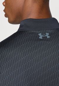 Crna atletska majica s teksturiranim uzorkom, kratkim ovratnikom i sivoj Under Armour logo na gornjem dijelu leđa. Izrađena od prozračne tkanine.