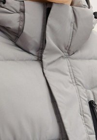 Szara kurtka puchowa z wysokim kołnierzem, o gładkiej fakturze, z kieszeniami na suwak i przeszyciami ocieplającymi.