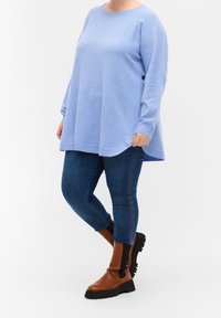 Blauwe lange mouwen sweater met een ronde zoom, gecombineerd met donkere jeans en bruine enkellaarsjes met zwarte zijkanten.