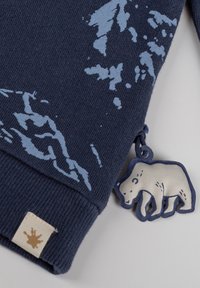 Felpa blu navy con motivi di montagna azzurri. Include un'etichetta a forma di orso e un'etichetta beige vicino al polsino.