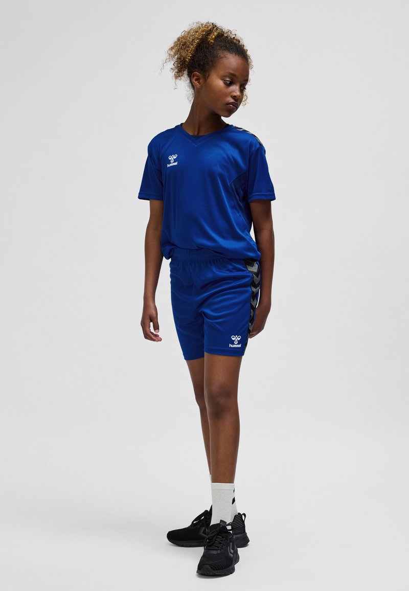 Blaues Sportshirt und Shorts mit Logo, mit V-Ausschnitt, kurzen Ärmeln und schwarzen Seitenakzenten. Dazu schwarze Turnschuhe und weiße Socken getragen.