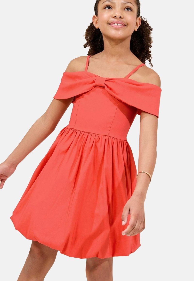 Abito corallo con design off-shoulder e dettaglio a fiocco nel collo. Gonna a campana, tessuto arricciato e spalline sottili per supporto.