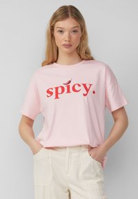 Hellrosa Baumwoll-T-Shirt mit kurzen Ärmeln, das das Wort "spicy" in fetter roter Typografie und einem kleinen roten Chili-Accent zeigt.