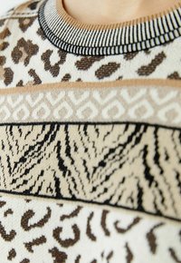 Strickpullover mit Leoparden- und Tiger-Mustern in Beige, Braun und Schwarz. Runder Kragen mit gestreiftem Rand und kontrastierenden horizontalen Streifen.