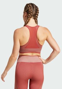 Ribbed sports bra in rusty red with racerback design and mesh texture. Matching high-waisted leggings feature a gradient pattern.