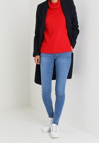 Punainen ribbed-kerrospaita, tummansininen takki, siniset kapeat farkut, valkoiset lenkkarit. Tyylikäs muotoilu, jossa on näkyvää tekstuuria neule- ja farkkumateriaaleissa.