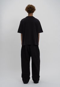 Melna lielizmēra T-kreklā un brīvā piegriezuma melnās biksēs, kas izgatavotas no mīksta auduma ar gludu tekstūru. Vienkāršs dizains bez redzamām rakstām vai akcentiem.