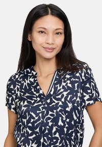 Blusa blu navy con motivo a foglie bianche, maniche corte e scollo a V, con un dettaglio di bottone davanti per un aspetto curato.