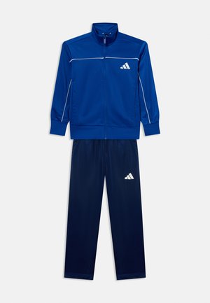 Blauer athletischer Trainingsanzug mit Reißverschlussjacke und passenden Hosen, mit weißem Logo auf Brust und Bein sowie weißen Paspeln an den Ärmeln.