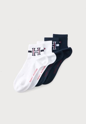 Zwei Paar Knöchelsocken, eines weiß und eines marineblau, jeweils mit einem "H" Logo und "Tommy Hilfiger" Text in Rot am Fuß.
