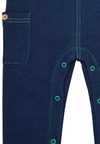 Pantaloni in denim blu navy con cuciture verdi, tasca laterale con bottone di legno e chiusure a scatto in fondo per un accesso facile.