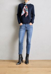 Maglione navy con scollo ampio, sciarpa a righe blu chiaro e multicolore, jeans blu chiaro attillati e stivaletti neri alla caviglia con punte argentate.