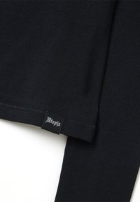 Schwarzes Langarmshirt aus weichem Stoff. Verfügt über einen genähten Saum und ein Etikett mit "Utopia" in weißem Text am unteren Saum.