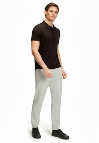 Czarna koszulka polo z kołnierzykiem w połączeniu z jasnoszarymi spodniami dresowymi. Dopełnieniem stroju są czarne trampki, tworząc casualowy styl.