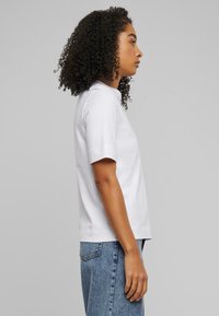 Hvit bomull t-skjorte med korte ermer, rund hals og en uformell passform, kombinert med lyseblå denimjeans, vist i profil.