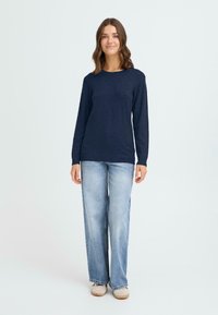 Marinblå långärmad topp tillverkad av mjukt tyg, ihop med ljusblå vida jeans. Stående modell, enkel design, utan synliga mönster eller detaljer.