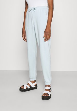 Personne portant un pantalon de jogging bleu clair avec taille à cordon et des sandales à plateforme blanches avec des brides épaisses.