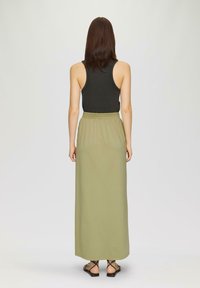 Zwarte tanktop gecombineerd met een lange olijfgroene rok. De rok heeft een elastische tailleband. Zwarte platte sandaaltjes maken de look af.