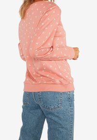 Sudadera rosa claro con patrón de hojas blancas, cuello y puños acanalados, ajuste relajado, combinada con jeans de mezclilla azul.