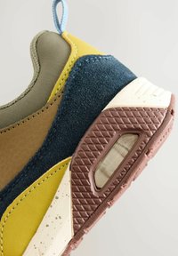 Sneaker aus einer Mischung aus olivgrünem, gelbem, braunem und marineblauen Materialien, mit einer strukturierten Wildleder-Oberfläche und einer Gummisohle mit Luftpolsterung.