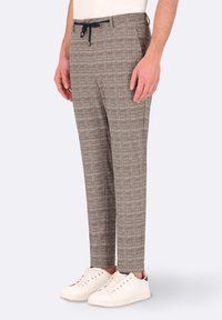 Pantaloni marroni a fantasia con vestibilità rilassata, vita con coulisse e tasche laterali, abbinati a sneakers bianche.