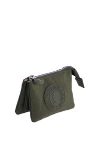 Funda con cremallera de color verde oliva, hecha de tela texturizada, con un logo circular en relieve en la parte delantera y un tirador de cremallera de tela.