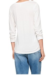 Vit långärmad skjorta med avslappnad passform, designad med uppvikta ärmar, mjuk textur och vid halsringning, matchad med ljusblå jeans.