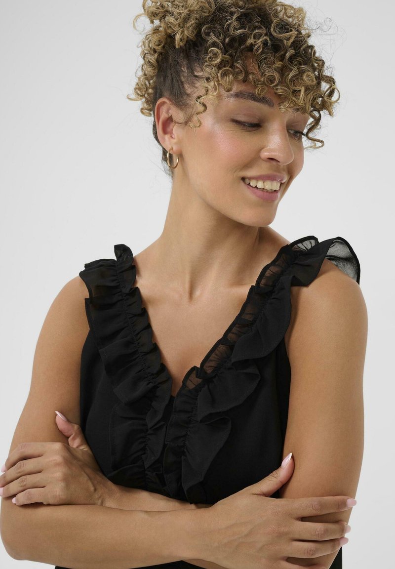 Black sleeveless top with ruffled detailing along the neckline, featuring sheer fabric accents. Smooth texture and fitted shape.