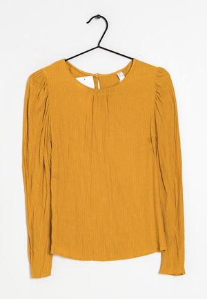 Long-sleeved mustard blouse with a round neckline, textured fabric, subtle pleats along sleeves, and a keyhole button closure at the back.