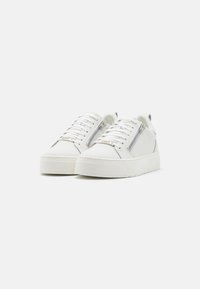 White sneakers with a smooth leather upper, featuring a side zipper, flat laces, and a chunky rubber sole. Subtle logo accent on the tongue.