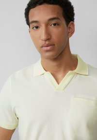 Koszulka polo w miękkim odcieniu żółci z teksturowanym wykończeniem, z dekoltem w serek i małą kieszonką na piersi. Kołnierzyk w kontrastującym jasnym odcieniu żółtego.