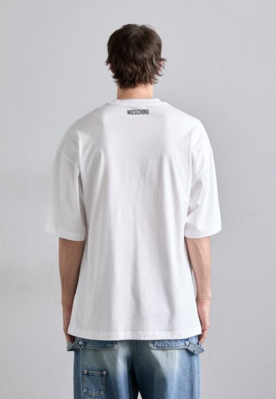 Valge lühikeste varrukatega t-särk, millel on lõdva lõikega, selja kaeluses must "MOSCHINO" logo. Kandmisel teksapükse.
