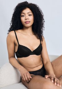 Σετ εσώρουχα από μαύρη δαντέλα με ελαφρώς επενδυμένο σουτιέν με κυματιστά άκρα και αντίστοιχο διάφανο σλιπ ψηλόμεσο. Λείο υλικό.