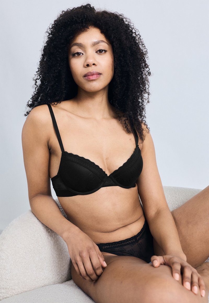 Σετ εσώρουχα από μαύρη δαντέλα με ελαφρώς επενδυμένο σουτιέν με κ υματιστά άκρα και αντίστοιχο διάφανο σλιπ ψηλόμεσο. Λείο υλικό.