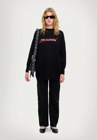 Black oversized sweatshirt with red text, paired with black wide-leg pants and simple black flats. Accessories include a large belt bag.