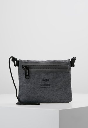 Grå skuldertaske i stof med sort lynlås og justerbar snorrem, mærket "anello" foran, vist på hvid overflade.