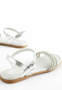 Zilveren metallic sandalen met een platte zool, een gevoerd beige voetbed, een verstelbare enkelband en kruislussen met kralenversiering.