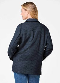 Textured black jacket with a collar, long sleeves, and a relaxed fit. The fabric displays a subtle woven pattern and appears mid-length.
