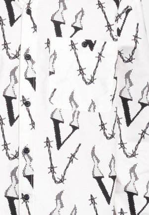 White shirt featuring a black geometric pattern of arrows and barbed wire. Contains a chest pocket and black buttons. Smooth fabric texture.