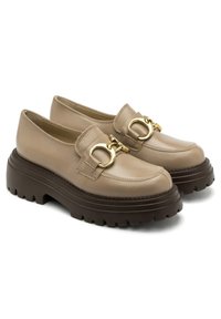 Beżowe skórzane mokasyny z grubą brązową gumową podeszwą. Posiadają złoty okrągły zamek na wierzchu oraz zaokrąglony kształt palców.