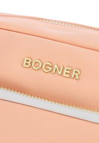 Sacchetto in tessuto color pesca con logo "BOGNER" in oro impresso e zip bianca con denti dorati. Texture liscia.