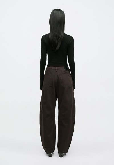 Camisola preta de manga comprida combinada com calças castanho-escuras largas. As calças apresentam bolsos grandes e uma superfície texturada, com pernas largas.