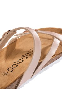 Sandalo con cinturino rosa chiaro e design incrociato, soletta in sughero e suola in gomma bianca. Presenta una texture simile alla pelle liscia e un dettaglio di branding.