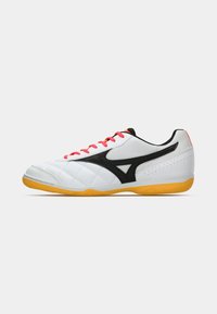 White athletic shoes with black accents, textured sides, and orange laces. Features a rubber outsole and quilted pattern on the toe.