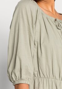 Světle zelená blůza s texturovaným, prošívaným vzorem. Disponuje kulatým výstřihem, nabíranými rukávy a elastickým pasem.