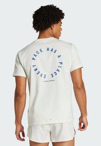 Lys grøn bomulds t-shirt med korte ærmer, der har blå cirkulær tekst på ryggen: "HVER LØB HAR SIT STED," med "ADIDAS RUNNERS" nedenfor.