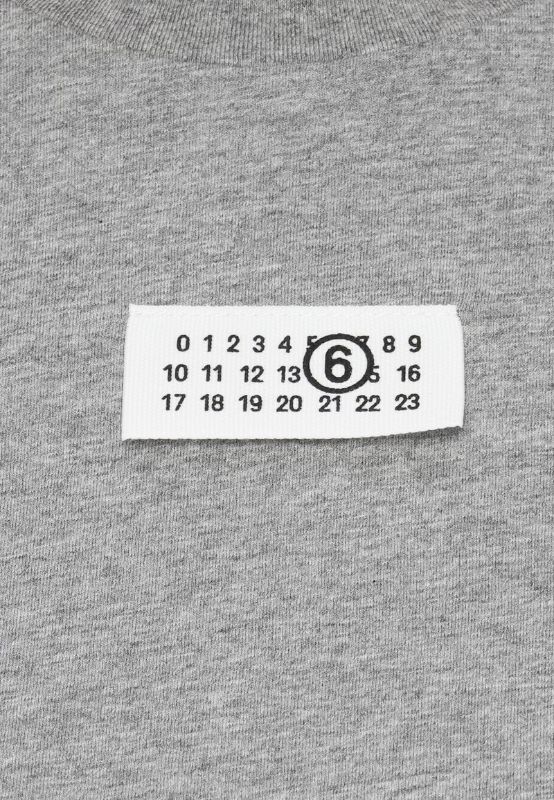 Gråt bomuldsstof med en tekstureret overflade, der har et hvidt tøjetiket med sorte tal og et indrammet "6".
