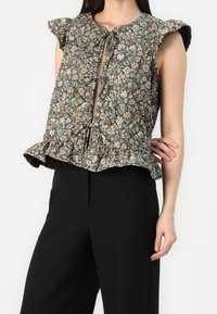 Top marrón con estampado floral, mangas con volantes, cierre frontal con lazo y dobladillo peplum, fabricado en tejido ligero. Combinado con pantalones negros.