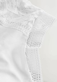 Witte kledingdetail met delicate kantafwerking en ingewikkelde patronen op een gladde satijnen basis, die een zachte textuur en verfijnd ontwerp toont.